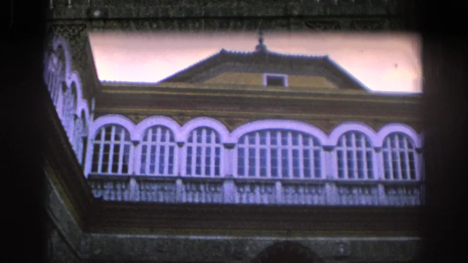 1966 Spain 8mm frame showing an upper roofline with tiled roofing, arched windows, decorative trim, and pale sky.
