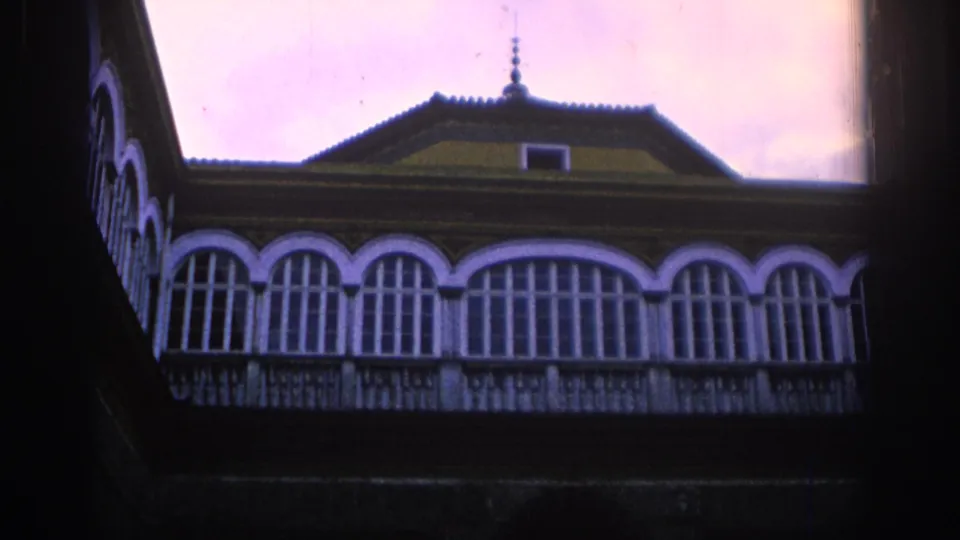 1966 Spain 8mm frame showing an ornate building facade with arched balcony windows, tiled roof, and shadowed courtyard foreground.
