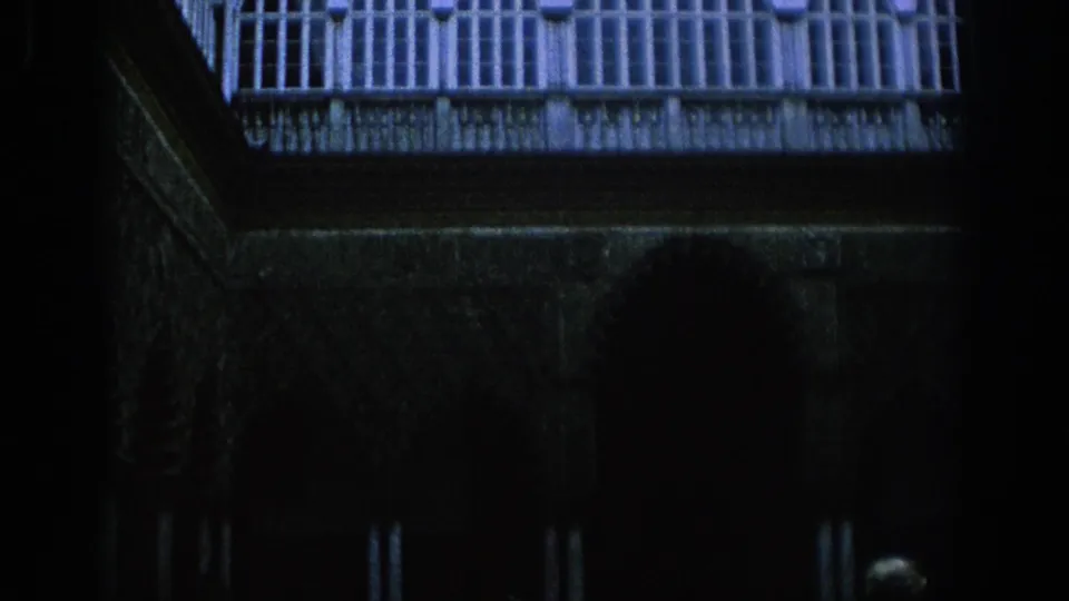 1966 Spain 8mm frame showing a dim historic courtyard with arched columns, balcony railings, and a woman near the lower edge.