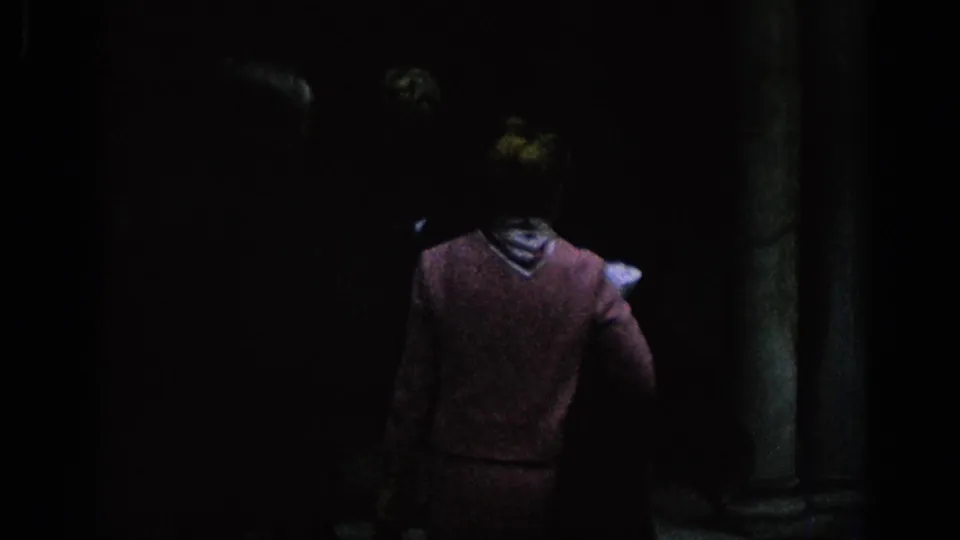 1966 Spain 8mm frame with a woman in a pink garment seen from behind as she enters a shadowed courtyard with columns.
