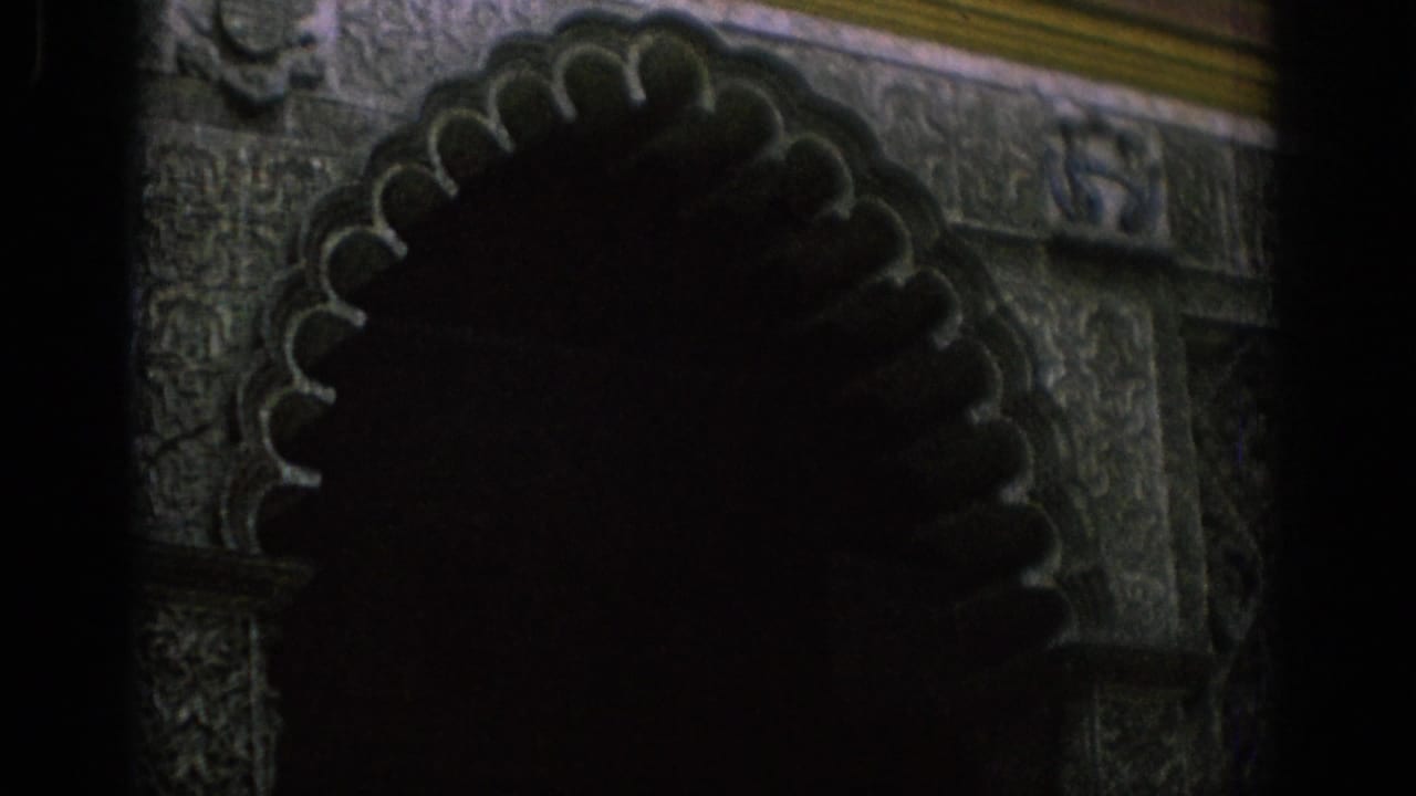 1966 Spain 8mm frame showing a shadowed visitor near an ornate carved archway at night.