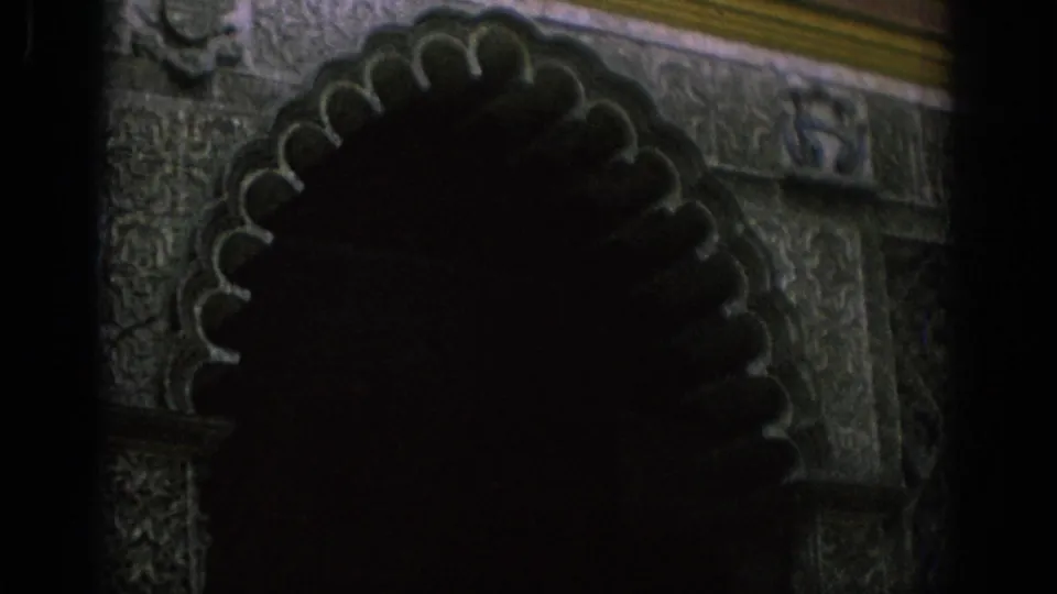 1966 Spain 8mm frame showing a shadowed visitor near an ornate carved archway at night.