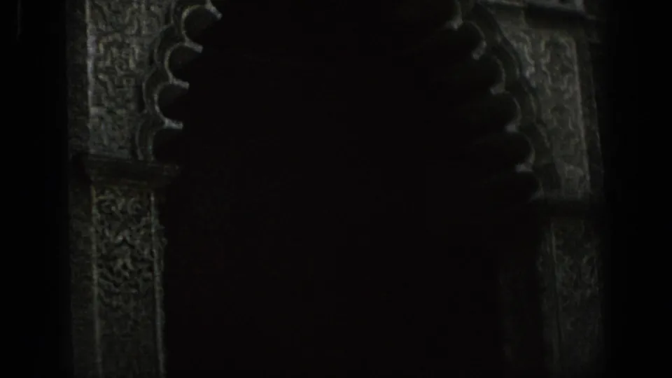Close 8mm view of a decorated Spanish archway, mostly in shadow with carved stone detail visible.