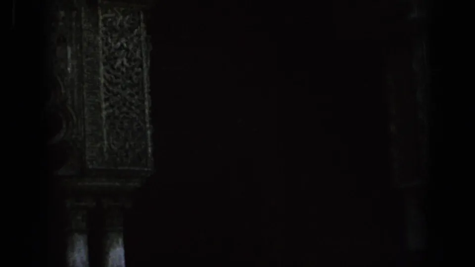 Very dark 8mm frame of a carved archway opening in Spain, with only faint architectural detail visible.