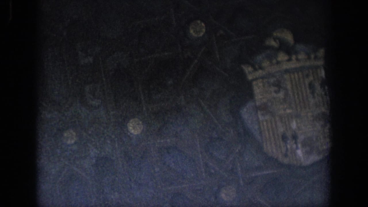 Underexposed 1966 Spain 8mm frame with faint stonework detail, heavy shadowing, grain, and dark film borders.