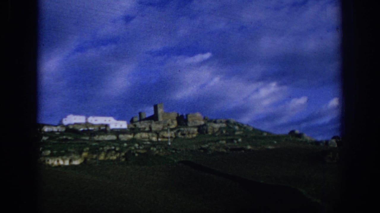 Hilltop stone ruins and white buildings under a deep blue clouded sky.