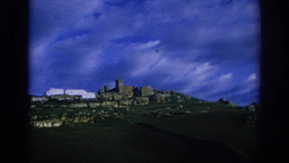 1966 Spain travel frame with hilltop stone remains, white structures, and dark foreground terrain under blue clouds.