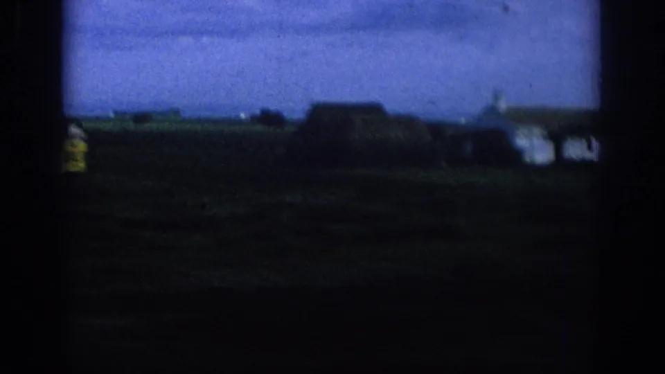 1966 Spain home-movie frame showing distant rural houses and open fields blurred by vehicle motion.