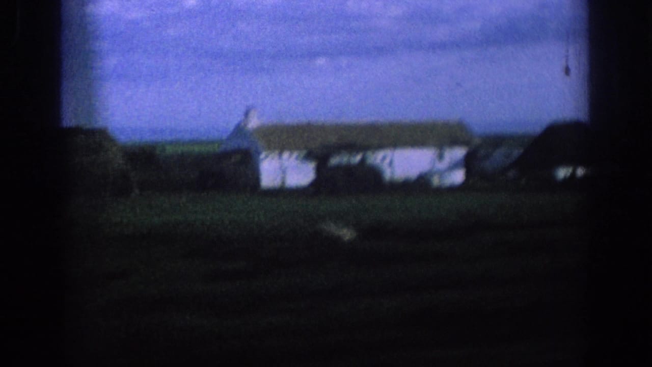 1966 Spain 8mm frame from a moving car, showing a white farmhouse and dark-roofed rural structure beyond fields.