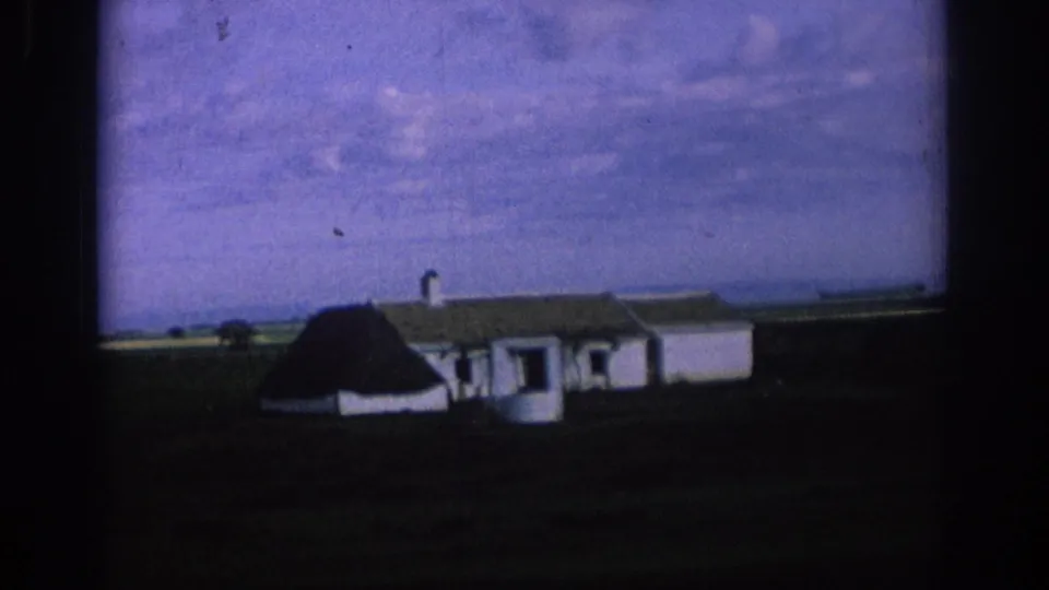 1966 Spain rural travel frame with a white farmhouse, dark thatched-looking roof, and low tiled extensions in open fields.