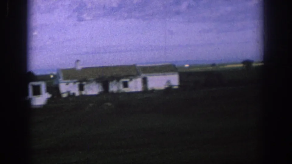 Final 1966 Spain frame with the white rural building sliding across the view, framed by dark film edges and blue-purple sky.