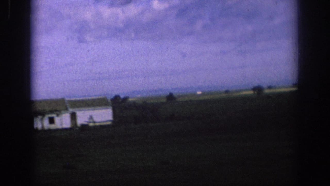 1966 Spain 8mm frame showing a distant white rural building, dark field, low horizon, and purple-shifted sky.