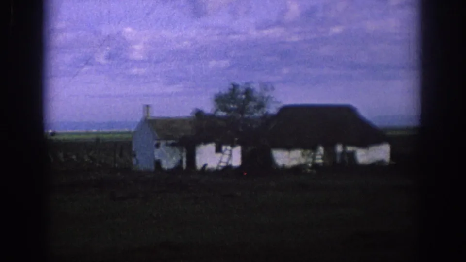 1966 Spain 8mm frame with a white farmhouse, small tree, dark roofline, open field, and distant horizon.