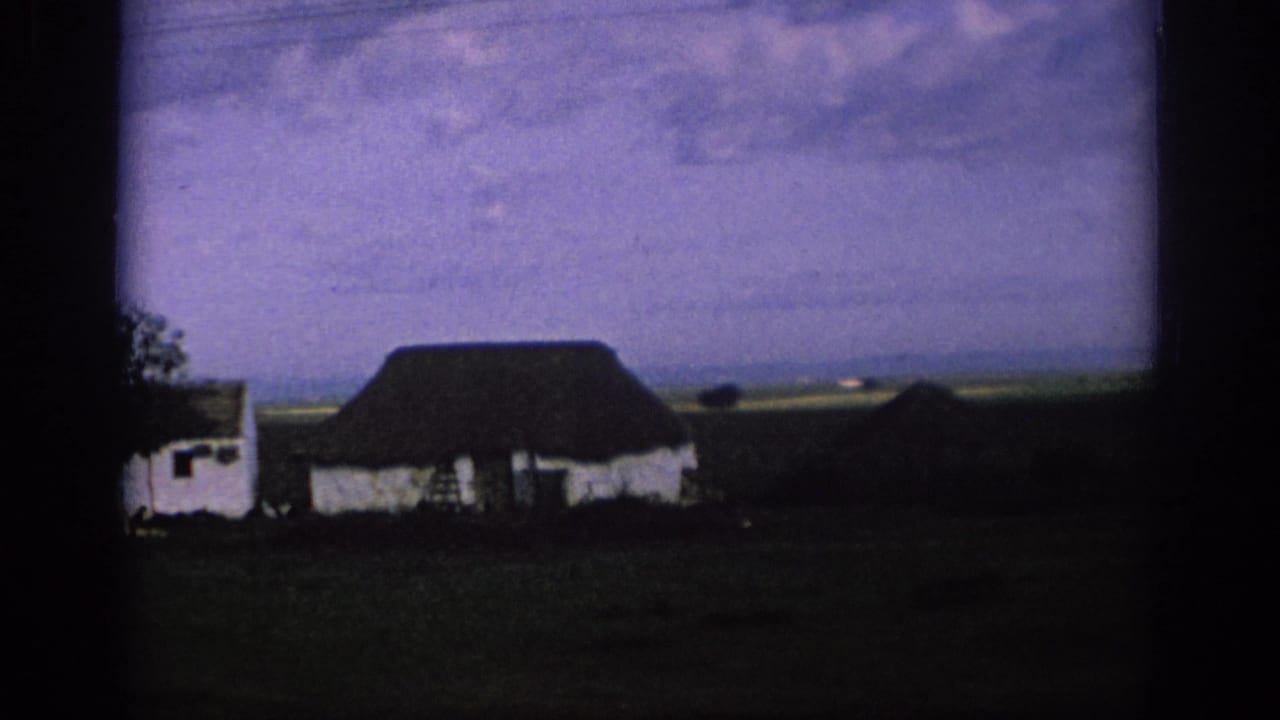 1966 Spain 8mm frame showing a low white rural building, dark roof, open land, and heavy film-frame borders.