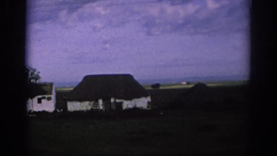 1966 Spain 8mm frame showing a low white rural building, dark roof, open land, and heavy film-frame borders.