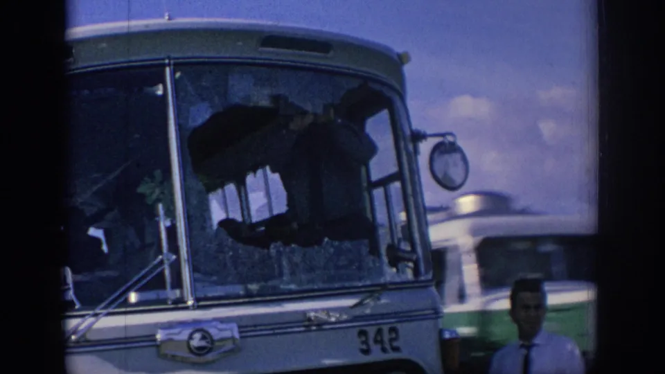 1966 Spain frame showing bus 342 with a shattered windshield, a man in a tie in front, and another vehicle passing in the background.