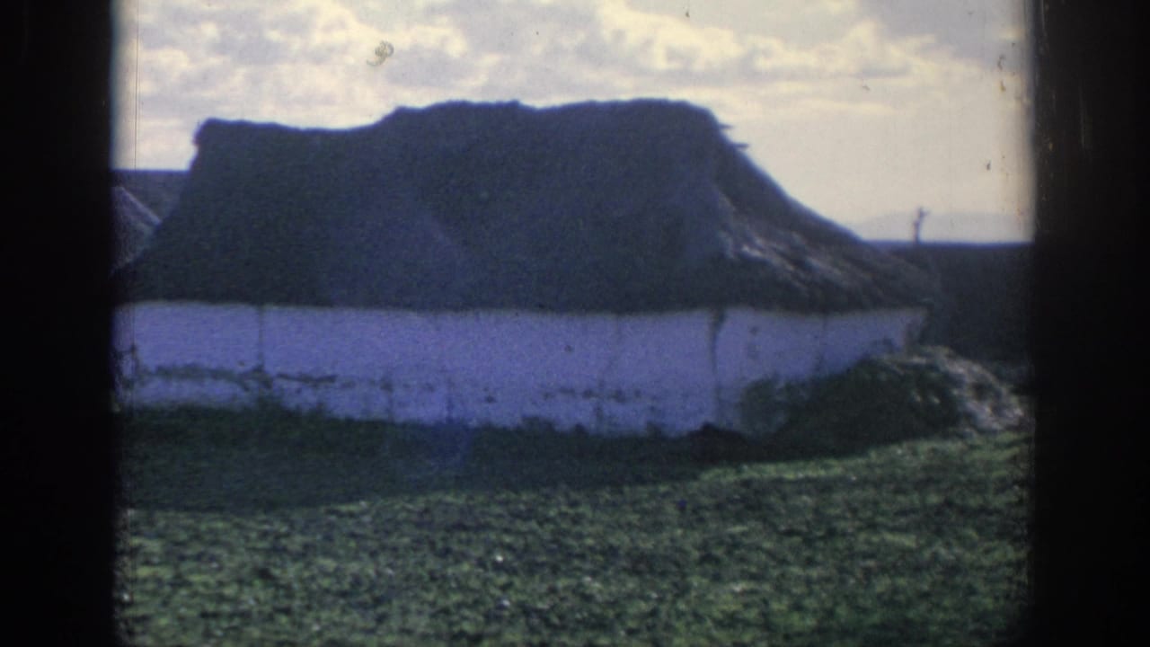1966 Spain 8mm frame looking toward a whitewashed rural building with a dark thatched roof under a bright sky.