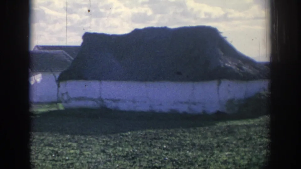 1966 Spain 8mm frame of a low white rural structure with a dark roof, grass in front, and soft handheld exposure.