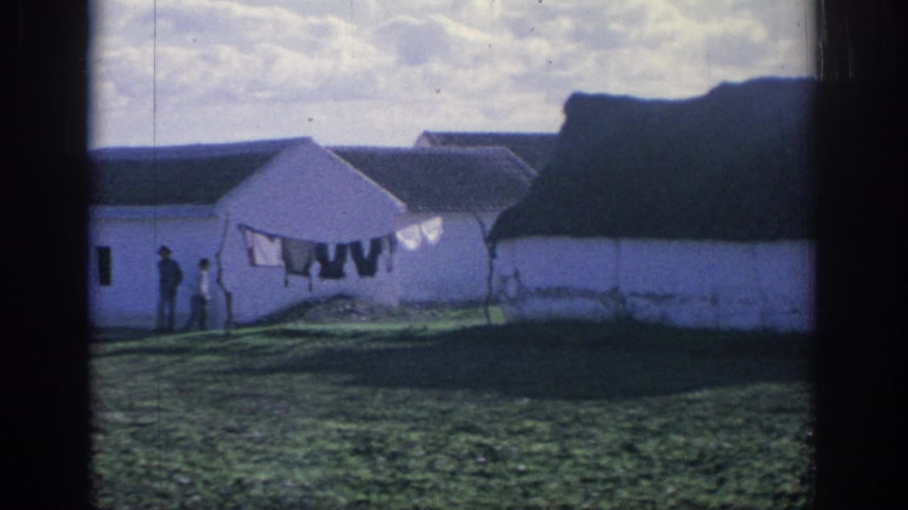 1966 Spain 8mm frame showing whitewashed farm buildings, a laundry line, and distant people in a grassy rural yard.