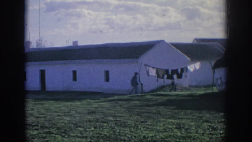 1966 Spain 8mm frame showing a long white farm building, small dark openings, laundry, and a distant figure in the yard.