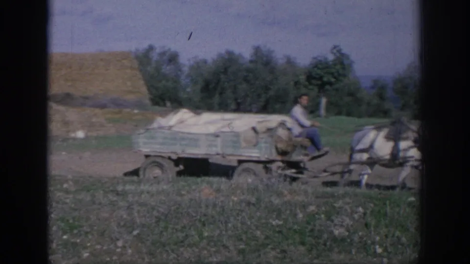 1966 Spain 8mm frame of a covered flat wagon and driver following a horse team across farmland.