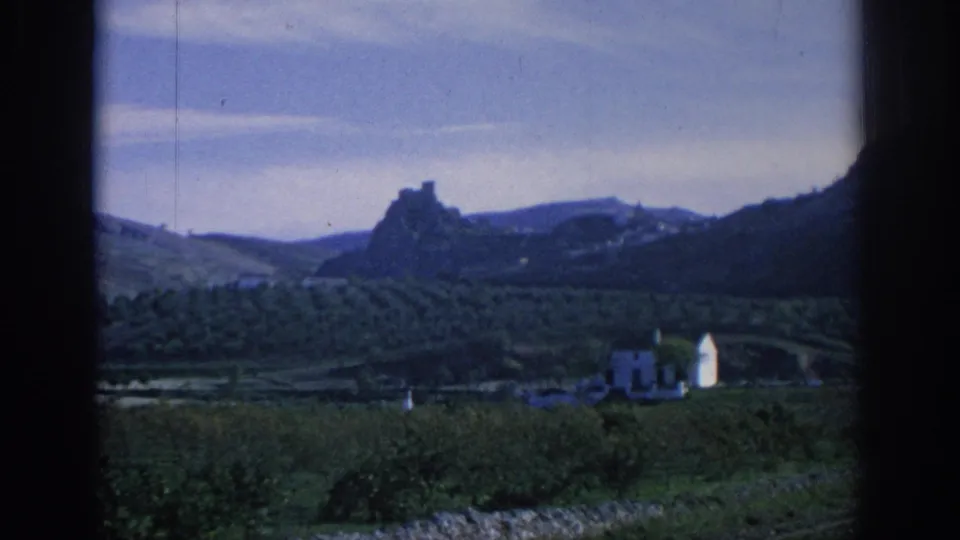 1966 Spain 8mm countryside view across cultivated valley fields toward distant rocky high ground and small white buildings.