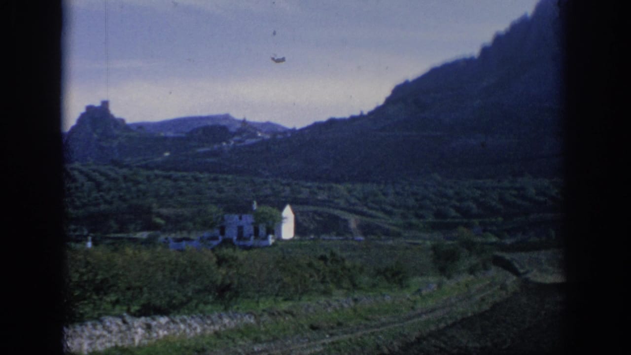 Terraced green valley with a white building, distant hills, and a dark window frame at the edges.