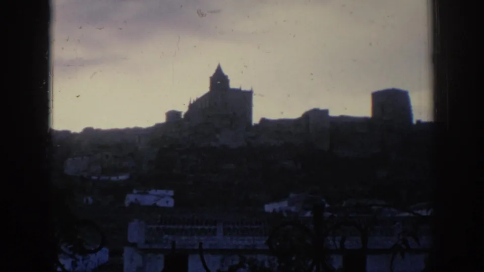 1966 Spain 8mm frame showing the castle and town as a dark silhouette against a pale evening sky, framed by vertical dark edges.