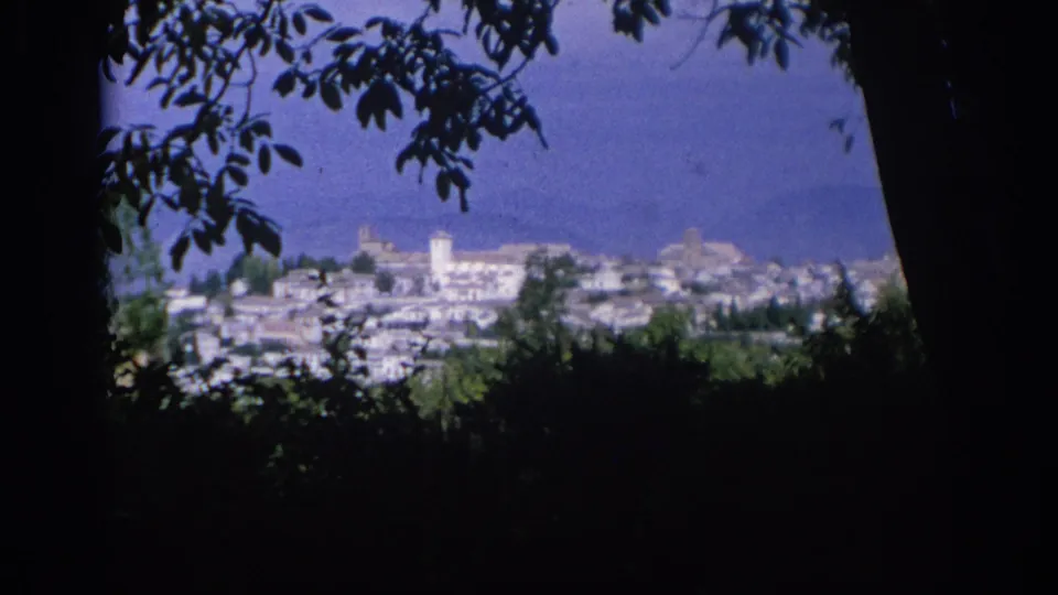 1966 Spain 8mm frame of a Mediterranean-looking town with white buildings, a tower, and distant hills seen through foliage.