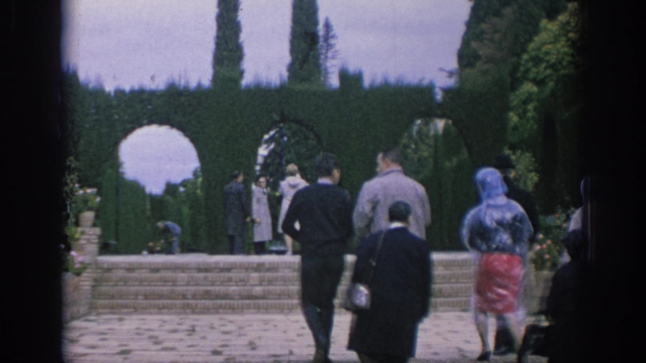 1966 Spain home-movie frame of tourists approaching brick steps, clipped hedges, and garden arches.