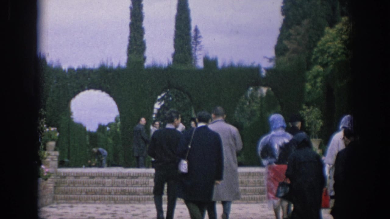 Visitors in coats stand and walk near steps below clipped hedge arches.