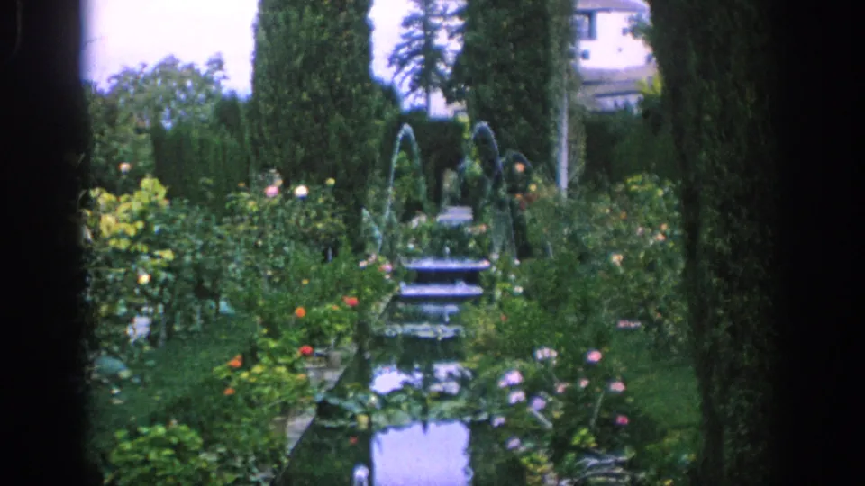 The Spain 1966 home-movie frame centers on formal garden fountains, reflective pools, flowers, hedges, and tall cypress trees.