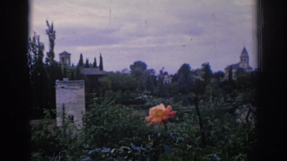 1966 Spain 8mm frame holding on the garden foreground and distant old-town skyline with a tower and cloudy sky.