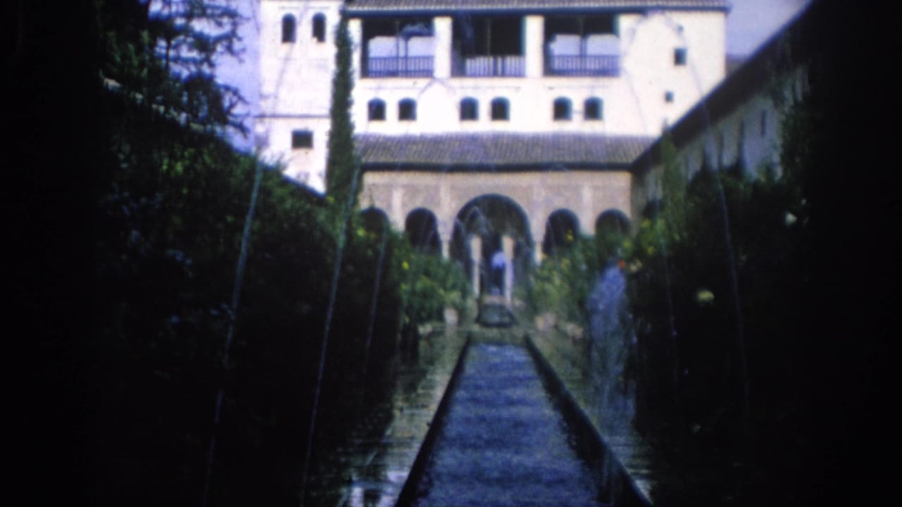 1966 Spain 8mm frame looking along a reflecting pool toward arched colonnades, balconies, cypress trees, and small visitors.