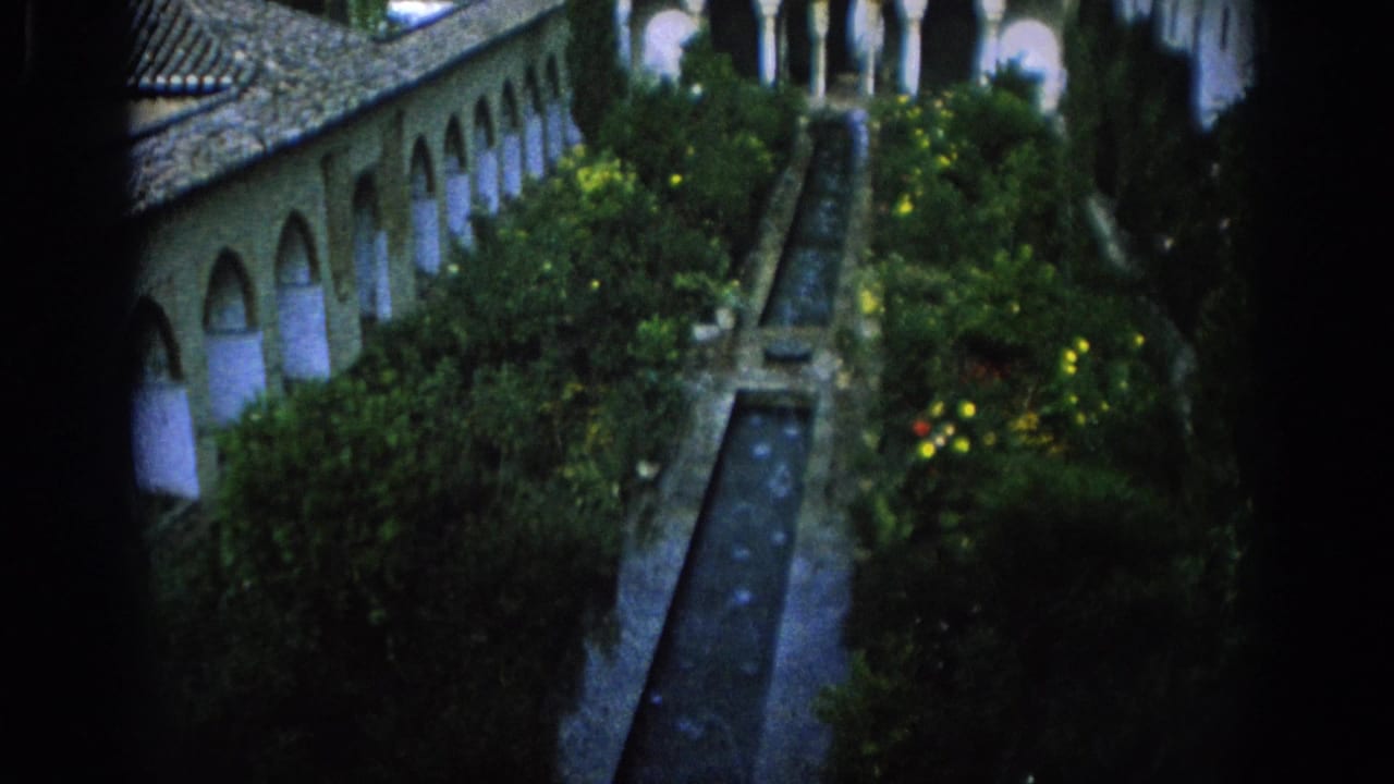 1966 Spain home-movie still with a formal courtyard garden, arched walkway, tile roof, and straight water channel viewed from above.