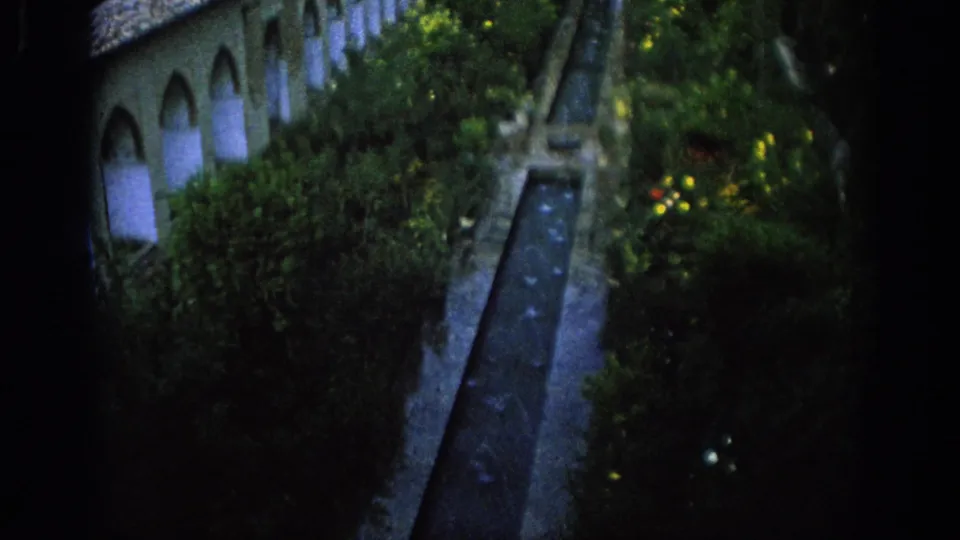 1966 Spain 8mm frame with the courtyard shifted lower in view, emphasizing the water channel, garden plants, arches, and roofline.