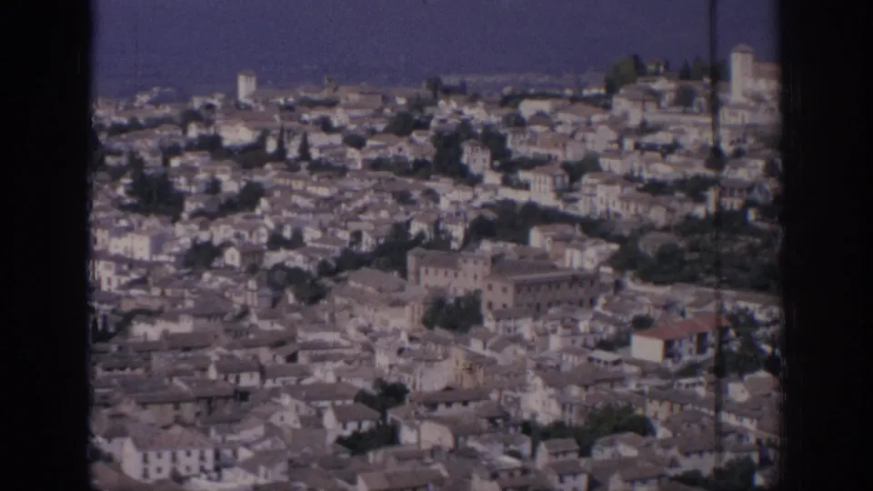 1966 Spain home-movie still showing a dense historic cityscape with pale buildings, tiled roofs, trees, and visible film borders.