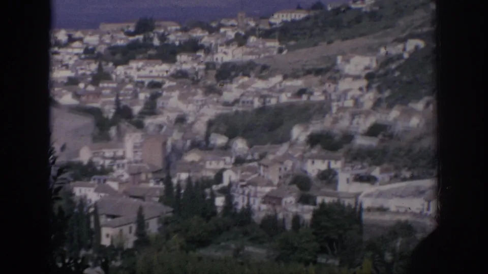 1966 Spain frame looking over a sloped townscape, with dense pale buildings, tiled roofs, trees, and visible 8mm frame edging.