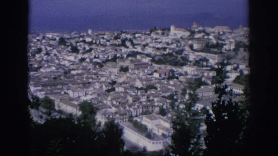 1966 Spain frame showing a broad town panorama from above, with pale buildings, terracotta roofs, trees, and dark 8mm frame borders.
