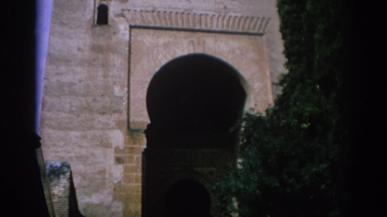 1966 Spain 8mm frame showing a weathered stone building with a Moorish-style arch, trees, and deep shadow around the entrance.