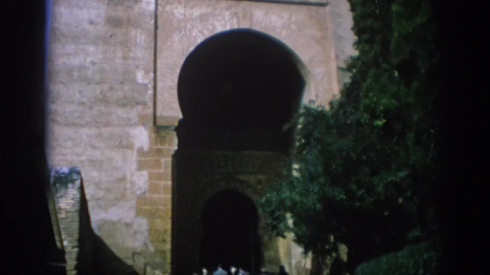 1966 Spain travel frame with a tall stone arch, leafy trees, a recessed doorway, and small distant visitors at the base.