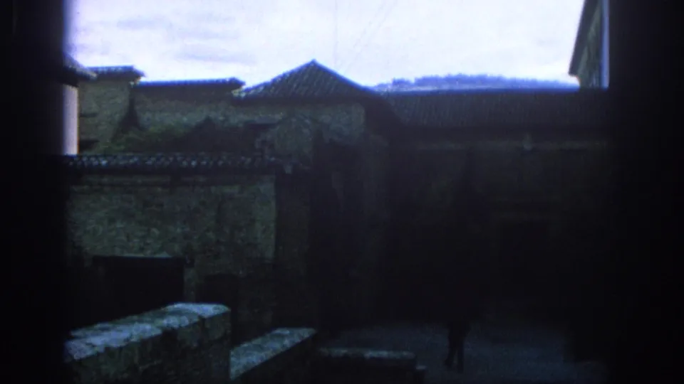 1966 Spain 8mm view through a shaded passage toward tiled rooftops, stonework, steps, and a small distant figure.