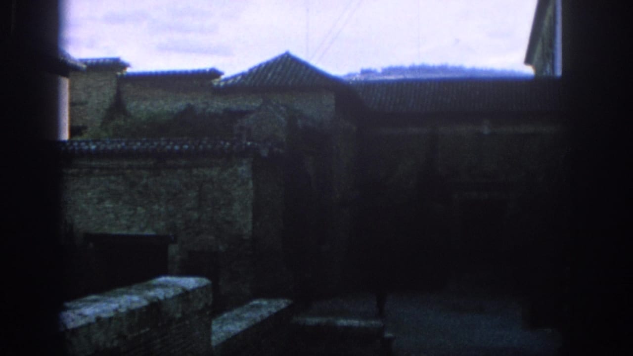Shadowed stone buildings with tiled roofs and a dark courtyard edge.