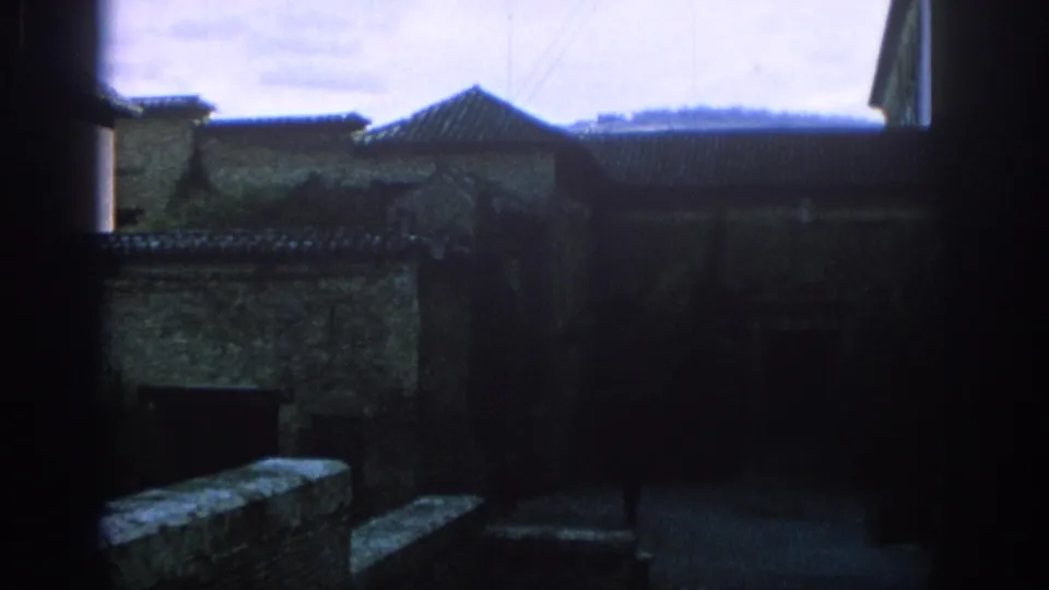 1966 Spain 8mm frame showing shadowed stone buildings, tiled roofs, and a dark exterior courtyard area.