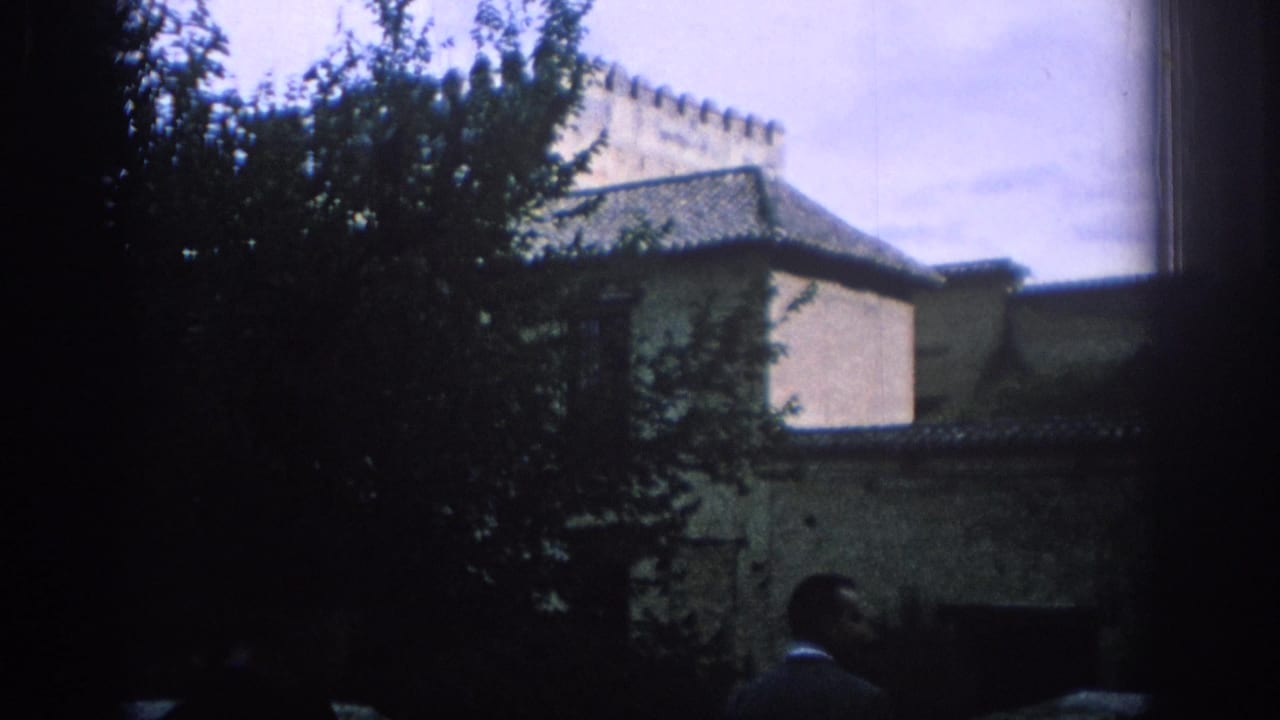 1966 Spain travel frame with a leafy tree, pale historic walls, tiled roofs, and a partial visitor in the foreground.