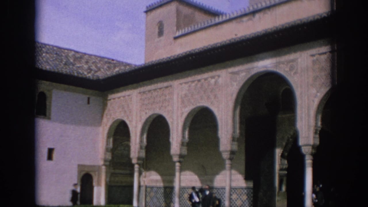 1966 Spain home-movie frame showing a Moorish-style courtyard arcade with ornate arches, carved wall panels, columns, and distant visitors.