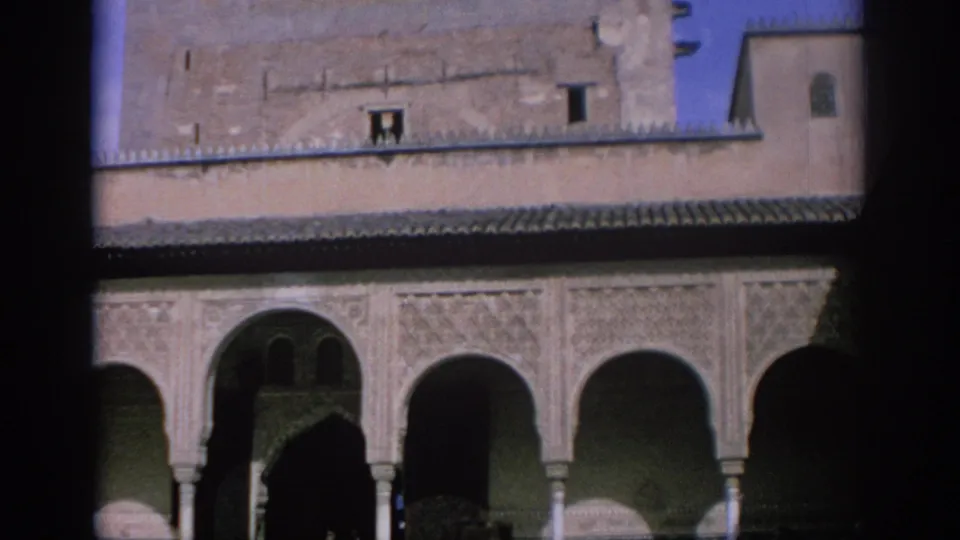 1966 Spain frame of a historic courtyard facade with carved arches, upper masonry, roof tiles, and shadowed openings beneath the arcade.