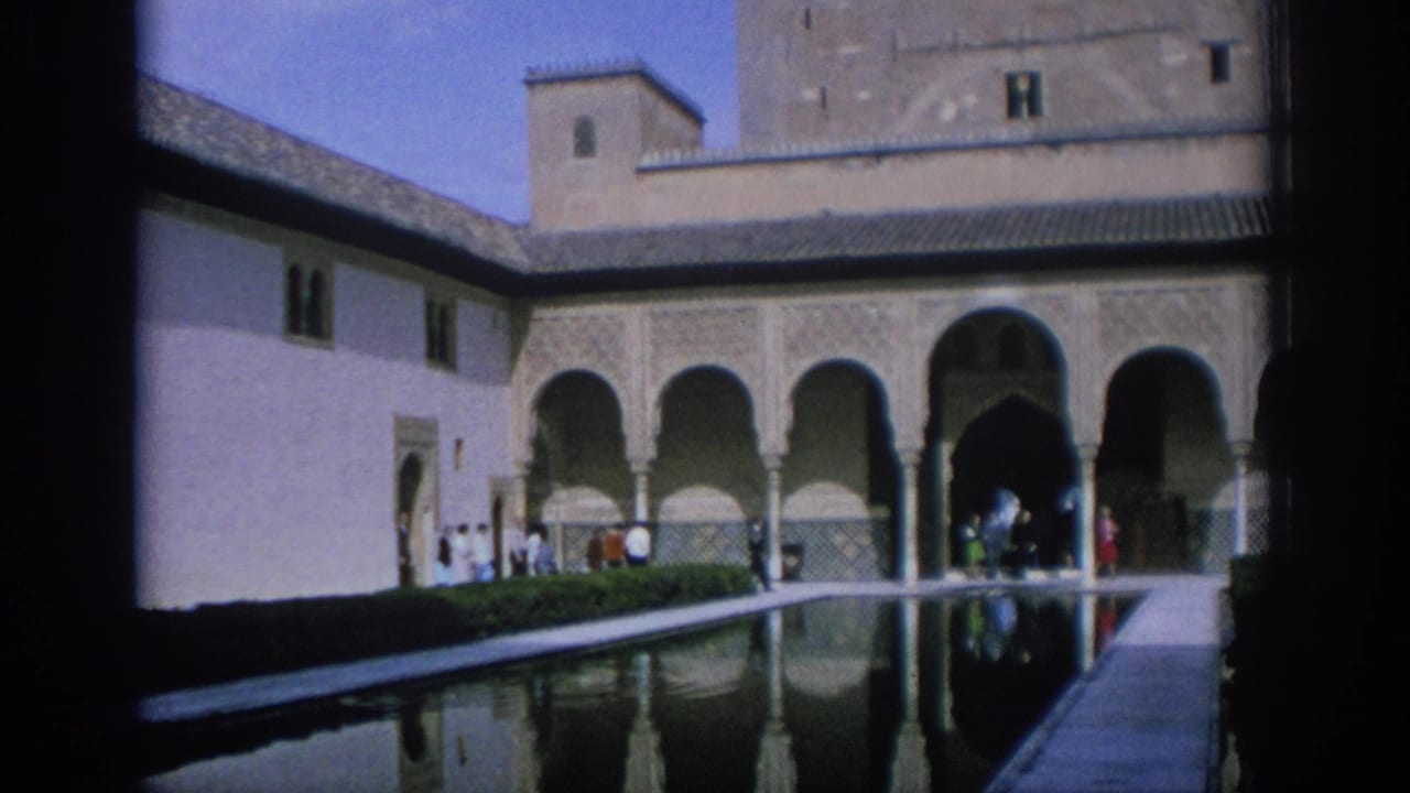 1966 Spain home-movie frame showing a long reflection pool, Moorish-style arches, and tourists moving through a historic courtyard.