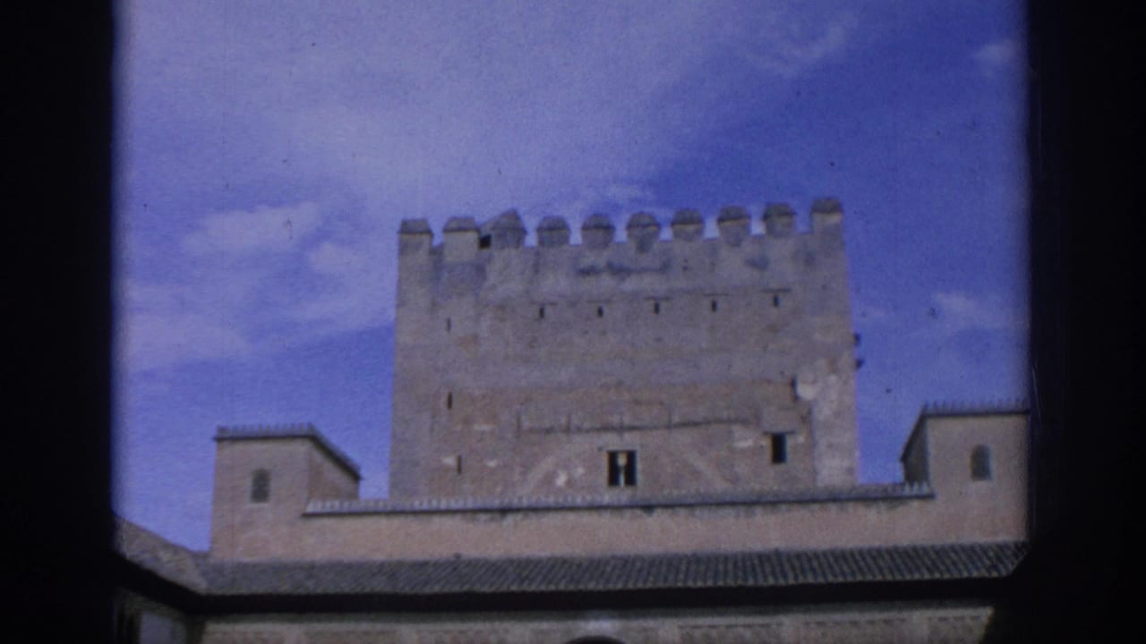 Crenellated stone tower rising above lower roofs against a blue sky.