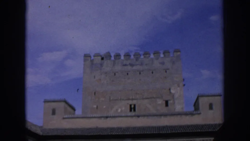1966 Spain home-movie view of a historic stone tower with battlements, small windows, and surrounding tiled roofs.